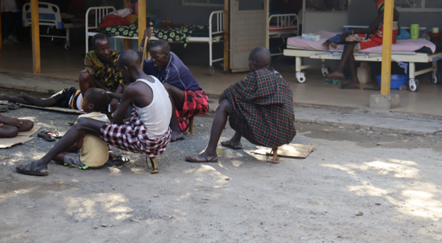 Eight-year-old Esekon Nangiro sits on the ground with his father, Nangiro Leyopo, outside LCRH treatment facility.