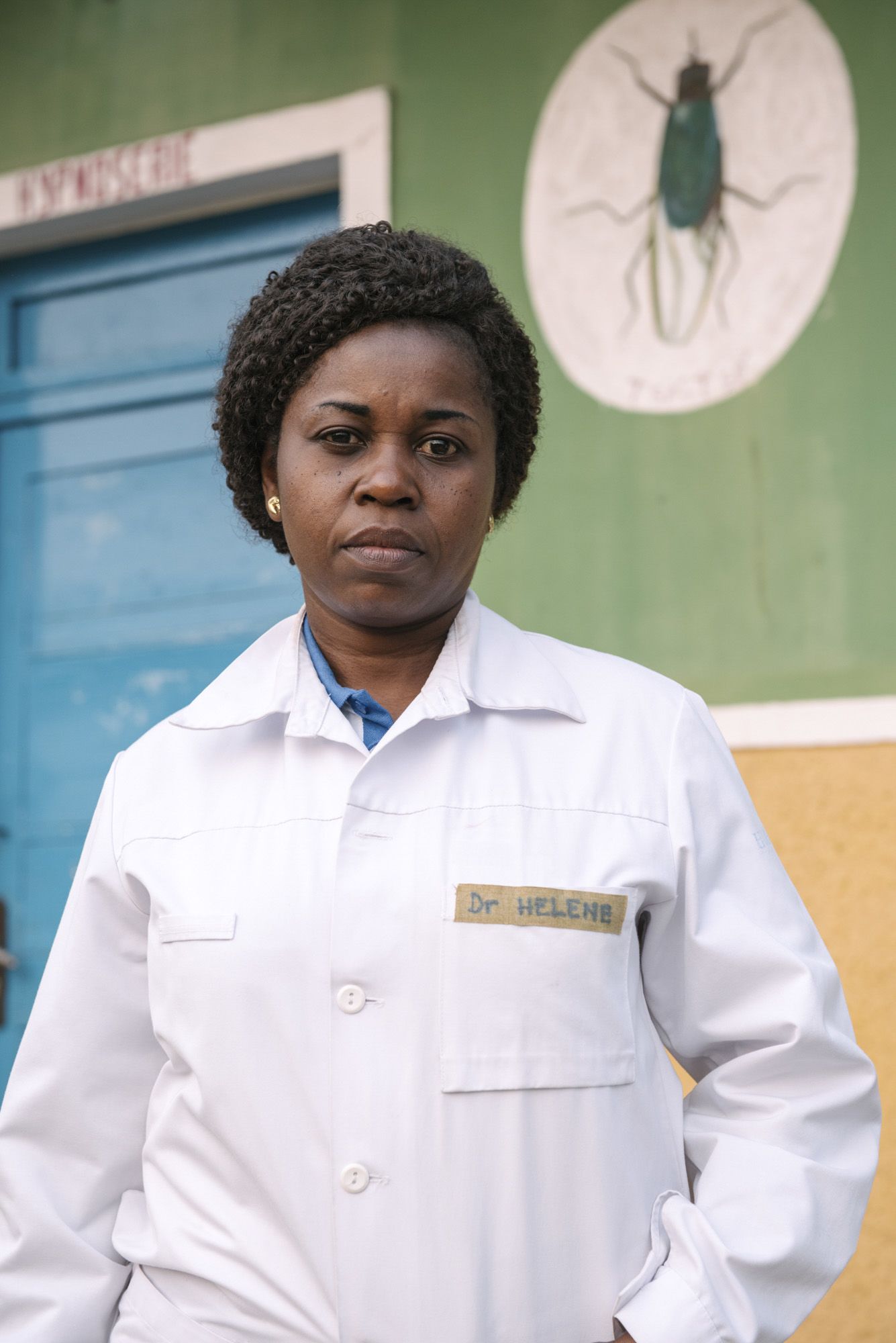 ツェツェバエのマークが描かれたアフリカ睡眠病病棟の外に立つエレーヌ医師